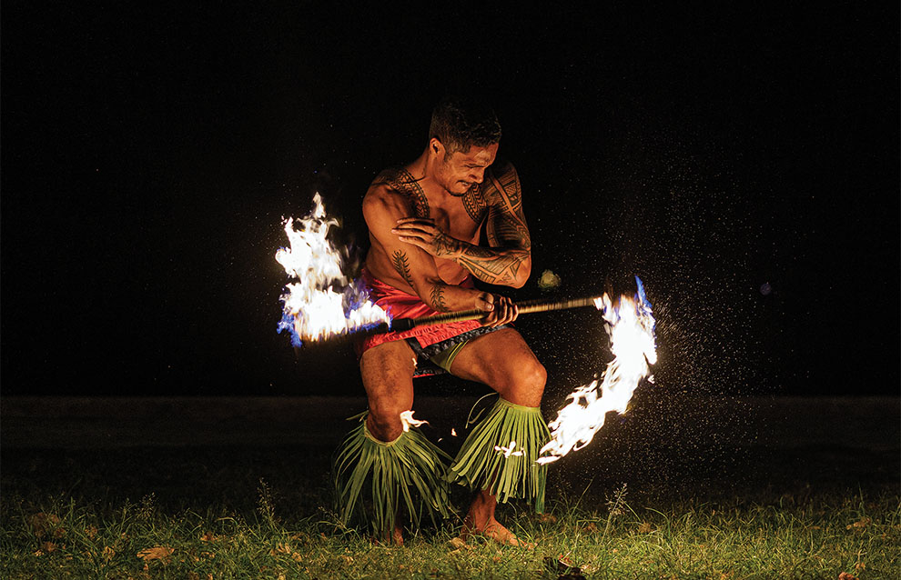 a tattooed fire artist performing at night in Hawaii dressed traditionally.